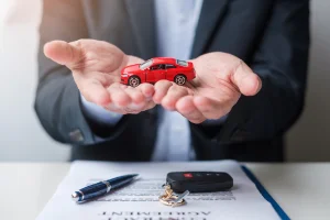 A red toy car held in protective hands representing extended warranty coverage
