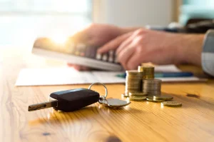 A wooden desk with a car key and a stack of change representing a lower car payment